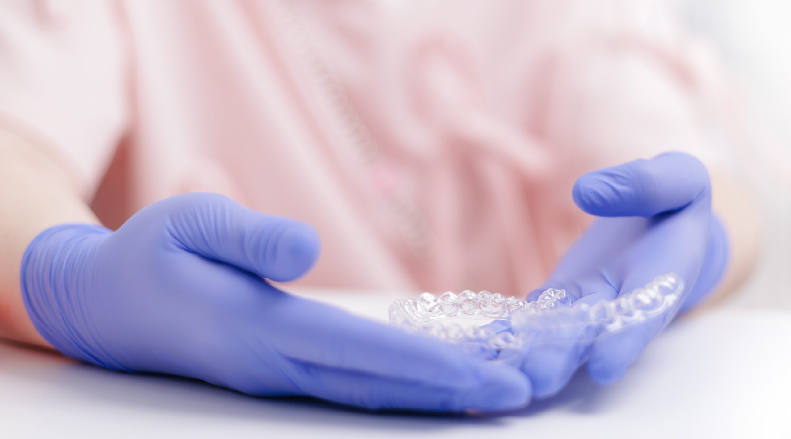 Dentistry concept, Gloved hands holding dental invisalign aligner on white table, orthodontic appliance to make teeth straight